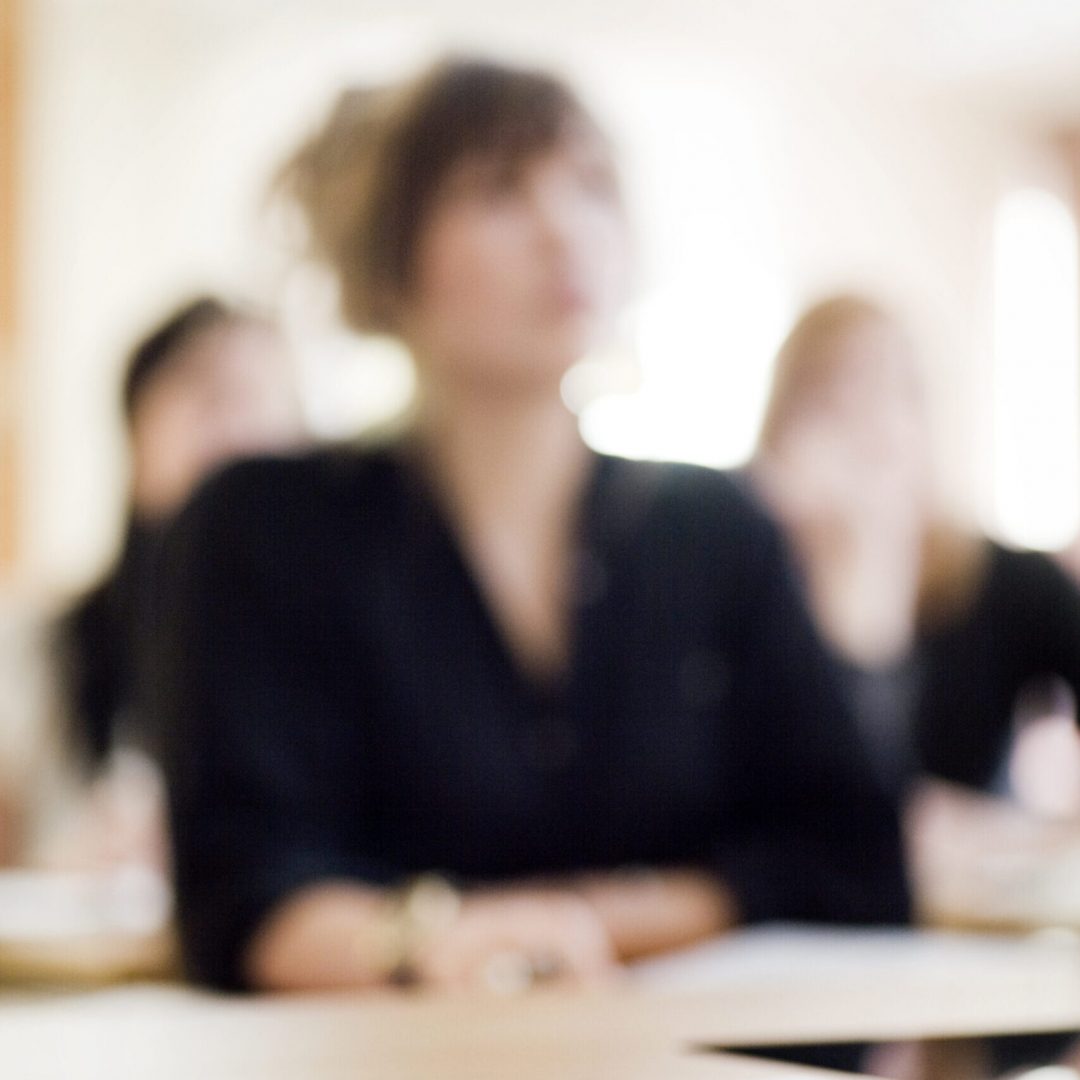 Close-up of pen and book on desk against woman sitting in classroom at university